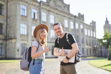 Mutlu öğrenciler kampüste başparmak işareti göstererek gülümsüyor