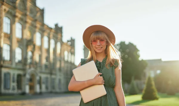 Happy student girl in hat and sunglasses holding laptop — Stock Photo, Image