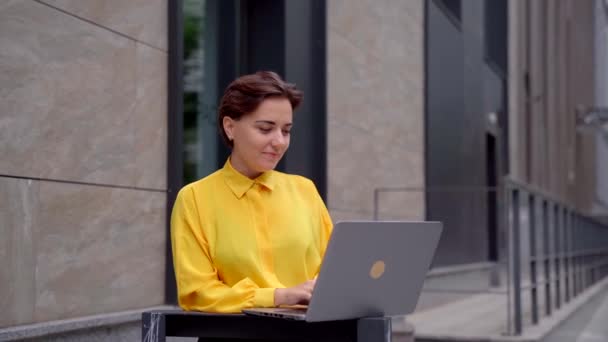 Jovencita en ropa formal usando portátil y mirando a la cámara — Vídeo de stock