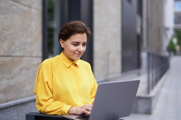 Confident serious businesswoman using laptop outdoor in city