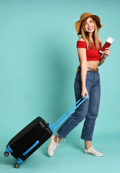 Young pretty woman with suitcase and passport on mint background