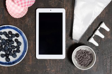 Tablet, ahşap arka plandaki kap kekler için malzemeler ve aksesuarlarla maket yapar.