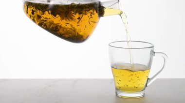 Çaydanlıktan şeffaf fincana bitki çayı dökülüyor.