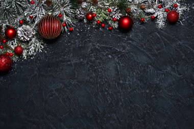 Koyu mavi arka planda kırmızı Noel süsleri olan çam dalları