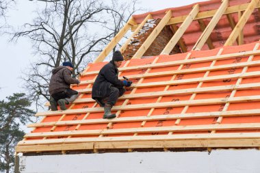 Irpin - Ukrayna - 13 Mart 2021: Çatı müteahhitleri kışın metal fayanslar için çatı döşeme ve buhar bariyerleri kuruyor.