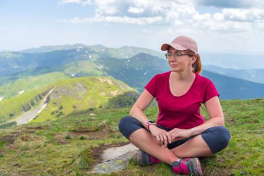 Genç bir kadın dağa uzun bir tırmanıştan sonra güzel doğanın arka planında dinlenmek için oturdu. Spor aktiviteleri. Sağlıklı yaşam tarzı.