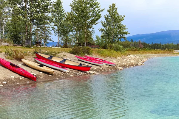 Una alineación de canoas y kayaks en una orilla de un lago de montaña — Foto de Stock