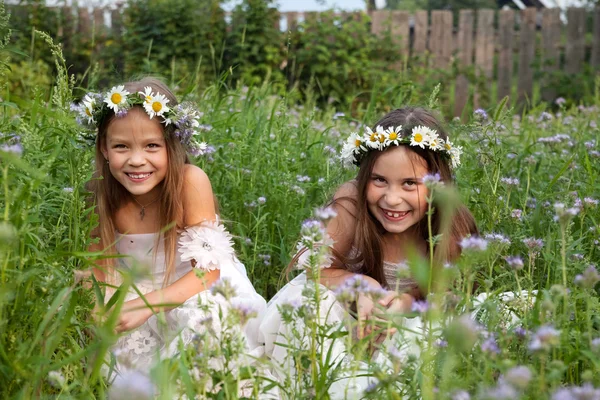 Niñas en coronas de manzanillas en la hierba riendo — Foto de Stock