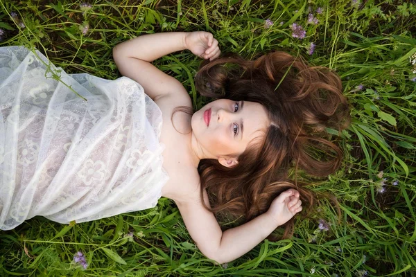 Маленька дівчинка в білій сукні лежить на траві — стокове фото