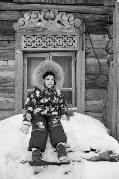 Menina de pé no inverno perto da velha casa de madeira e janela esculpida — Fotografia de Stock