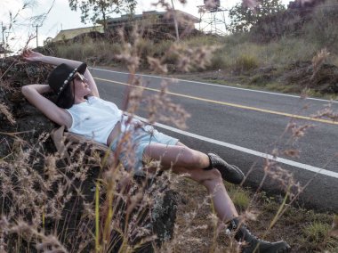 Sırt çantalı kız yolun kenarında dinleniyor ve gezintiyi bekliyor. Seyahat kavramı