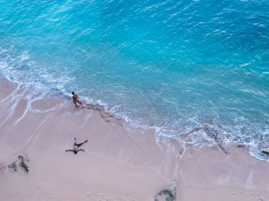 Endonezya 'nın Bali sahilindeki bir çiftin hava görüntüsü. Tatil ve macera. Plaj ve turkuaz su. Kumsaldaki İHA 'nın üst görüntüsü, masmavi deniz ve sakin bir çift. Seyahat et ve rahatla - görüntü