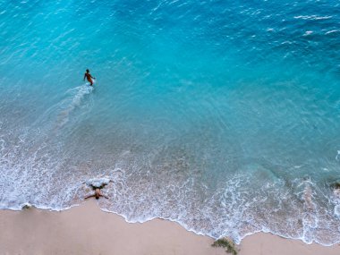Endonezya 'nın Bali sahilindeki bir çiftin hava görüntüsü. Tatil ve macera. Plaj ve turkuaz su. Kumsaldaki İHA 'nın üst görüntüsü, masmavi deniz ve sakin bir çift. Seyahat et ve rahatla - görüntü