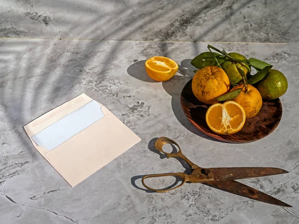 Sliced orange fruits with leaves, blank card on white table background in sunlight. Close up mock up blank white letterhead, long shadows and palm branch. Branding concept. Invitation, announcement.