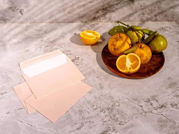 Sliced orange fruits with leaves, blank card on white table background in sunlight. Close up mock up blank white letterhead, long shadows and palm branch. Branding concept. Invitation, announcement.