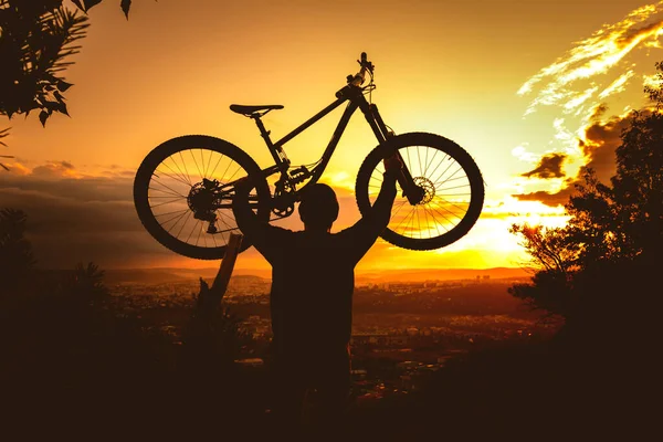 Silhouette di un mountain bike che tiene una bicicletta sopra la testa al tramonto. MTB, enduro, sfondo freeride. — Foto Stock