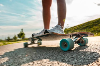Asfalt yolda güneşli bir günde hareket halinde olan uzun bir tahtanın geniş açılı bacakları. Dönen tekerleği kapat.