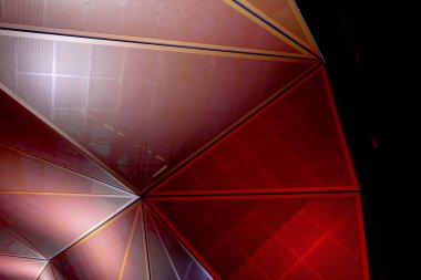 Modern mimari. Üçgen parçalardan turuncu ve kırmızı geometrik metalik yapı. Karanlıkta soyut arkaplan tasarımı.