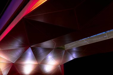 Modern mimari. Üçgen parçalardan turuncu ve kırmızı geometrik metalik yapı. Karanlıkta soyut arkaplan tasarımı.
