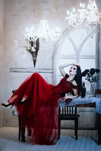 Bloodthirsty female vampire in red dress. Medieval interior — Stock Photo, Image