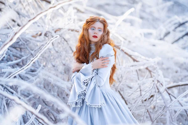 Mladá zrzka žena, princezna, kráčí v zimním lese v modrých šatech. — Stock fotografie