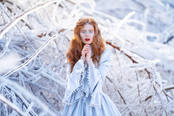 Young redhead woman, a princess, walks in a winter forest in a blue dress. — Stock Photo, Image