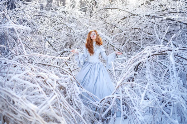 Jonge roodharige vrouw, een prinses, wandelt in een winterbos in een blauwe jurk. — Stockfoto