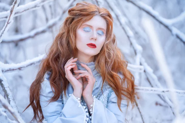 Jonge roodharige vrouw, een prinses, wandelt in een winterbos in een blauwe jurk. — Stockfoto