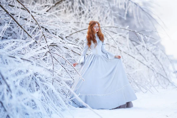 一位红头发的年轻女子，一位公主，穿着蓝色连衣裙行走在冬季的森林里. — 图库照片
