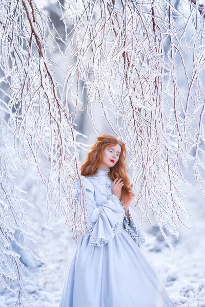 공주인 젊은 붉은 머리 여인이 푸른 드레스를 입고 겨울 숲 속을 걷고 있다. — 스톡 사진