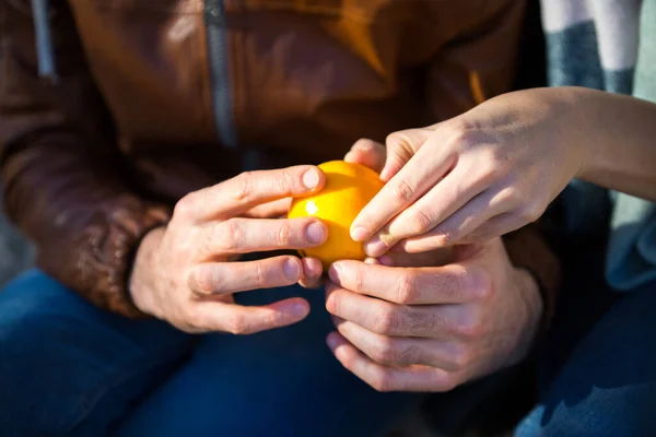 Genç çift güneşli bir günde portakal soyarlar. İnsan eli yakın çekim. Aşk ve sağlıklı yaşam tarzı kavramı. Açık havada doğal vitaminler yiyor. İşbirliği ve takım gerçek hayatta çalışır.