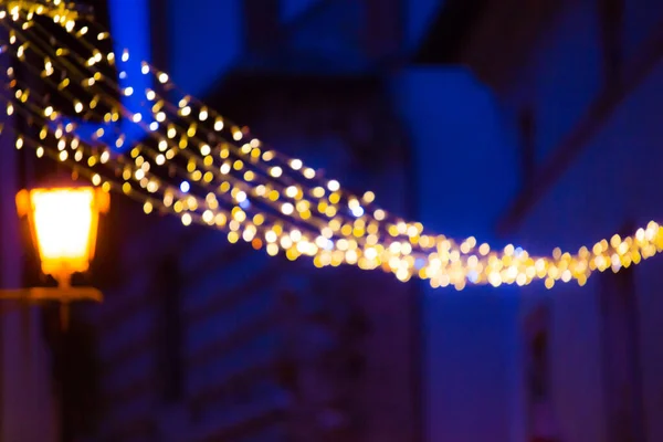 Fundo de borrão com iluminação de ano novo e luz de rua na noite. Luzes brilhantes desfocadas na escuridão. Noite mágica da véspera de Natal. Design de padrão de efeito artístico para papel de parede. — Fotografia de Stock