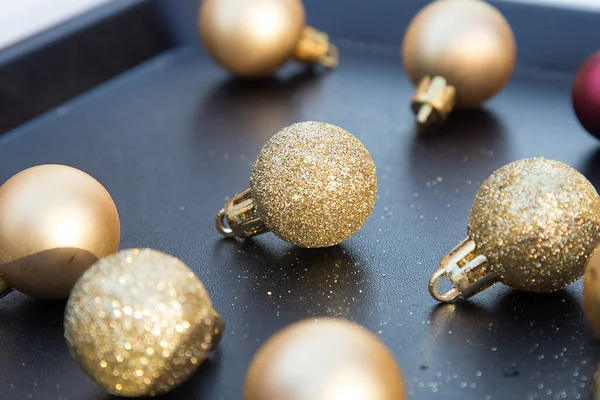 Siyah tepside küçük altın parıldayan Noel topları. Yeni yıl süslemeleri. Xmas oyuncaklarını kapatın. Tatil menüsü. Duvar kağıdı ve kartpostal resmi. Çam ağacı süslemeleri. Sosyal mesafe. Parlak