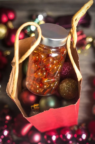 Dikey yeni yıl resmi. İçinde balık yağı hapları olan kırmızı hediye poşeti ve arka planda Noel topları. 2021 'i kutluyoruz. Yeni salgın gerçeklik mevcut. Hediye için bir fikir. D vitamini