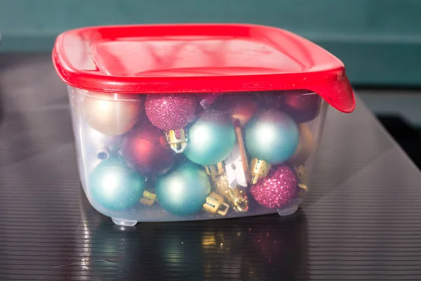 Golden, tiffany and burgundy Christmas balls packed for keeping in a transparent plastic food container with red cover on black table. Storage of new year decoration. Space management Stock Photo