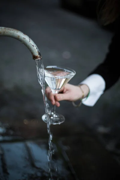 Kristal camlı el. Roma 'da geleneksel sokak çeşmesi. Antika su kemerinden taze su. Kadının elinde martini kristal bardağı var. Arka plan bulanık. İçme suyu. Tazelik kavramı.