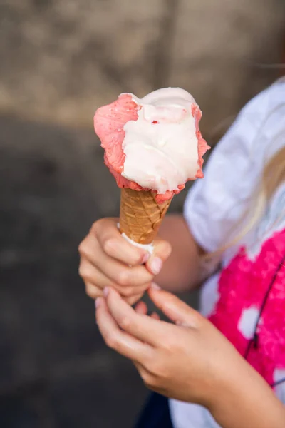 child hand holding ice cream cone, pink and white scoops melting under sun, waffle cone gripped by small fingers, sticky drips