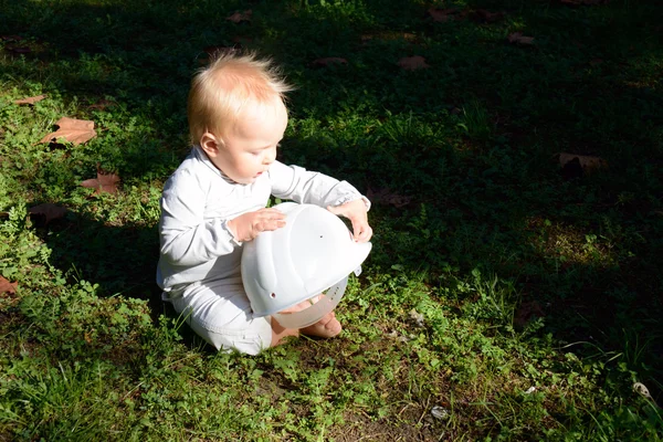 Baby is examining a hard cap outdoors on the ground — Stock Photo, Image