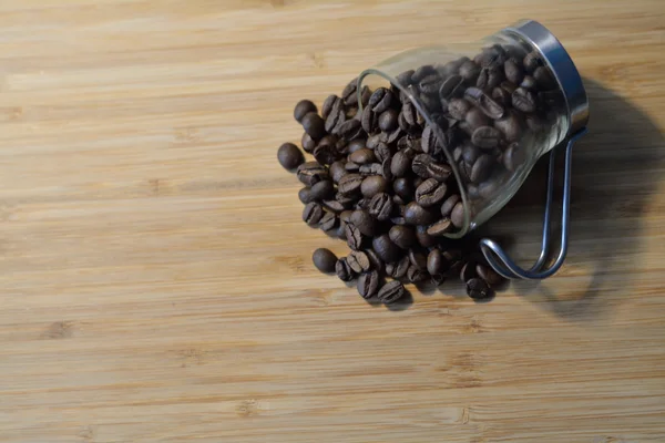 Small glass cup lis on a wooden table with coffee beans — Stock Photo, Image