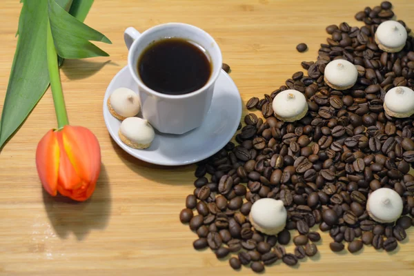 Coffee beans, cup of coffee, small pastry and a tulip — Stock Photo, Image