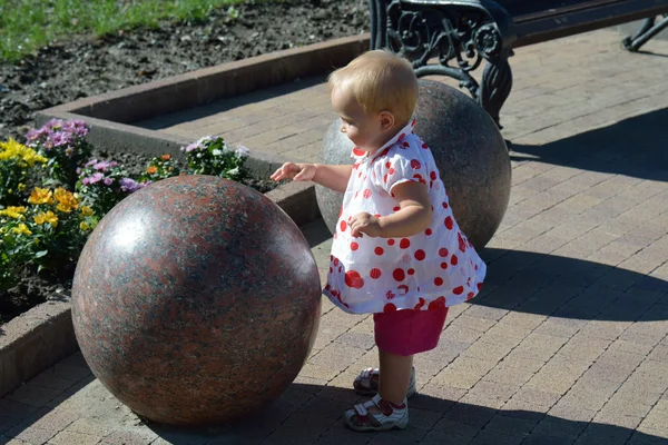 A cute baby girl standing next to the stone ball in summer — Stock Photo, Image