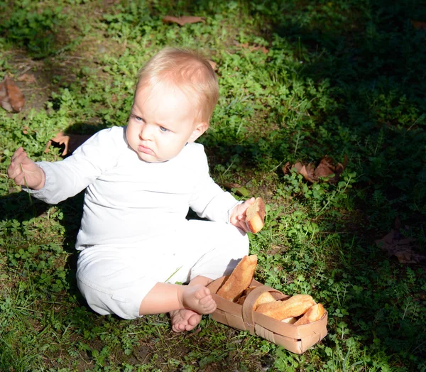 Girl with a rusk sits in white clothing next to the basket — Stock Photo, Image