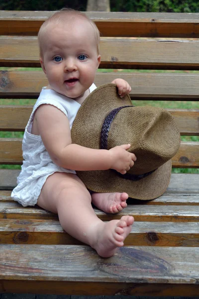 An infant sitting on the bench with the hat — Stock Photo, Image