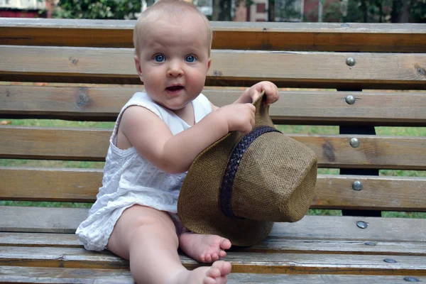 Dziewczynka w wielkim kapeluszu siedząc na ławce — Zdjęcie stockowe