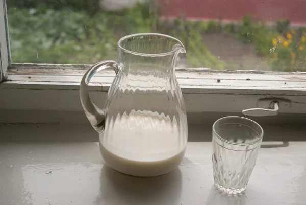 Jug of milk and a glass on a windowsil — Stock Photo, Image