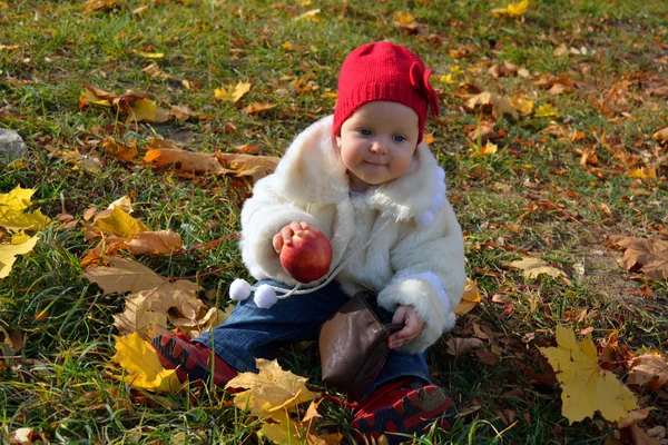 Cute little girl sitting in autumn leaves with an apple — Stock Photo, Image