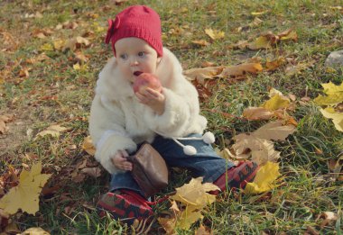 Kırmızı şapkalı açık havada elma yiyen küçük kız