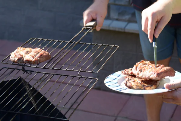 Men taking the barbecue off the grill, and outting it into a pla — Stock Photo, Image