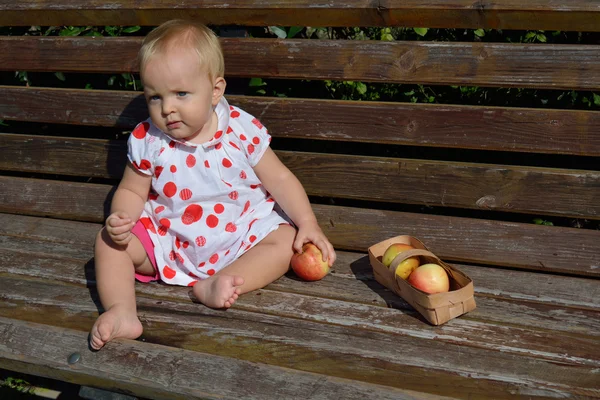 A baby girl sits on a bench with an apple — Stock Photo, Image