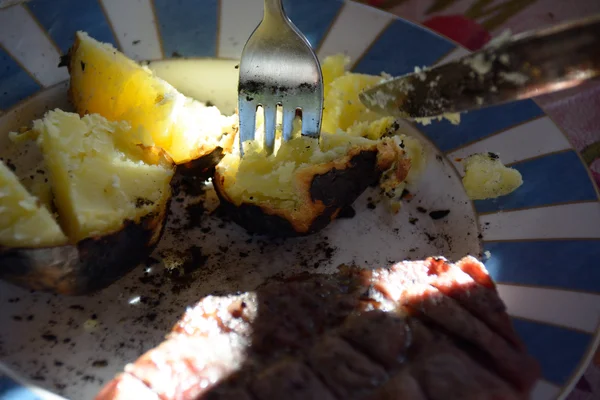 Печеная картошка и мясо на тарелке — стоковое фото